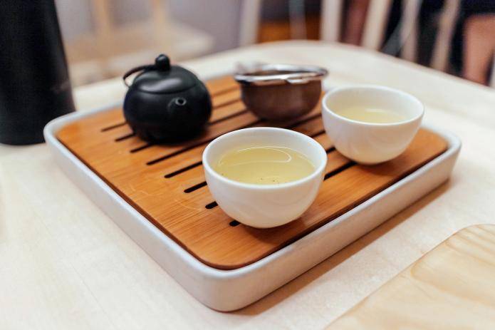 特写的绿茶设置在杯子上的小木盘子与水壶和教练机。