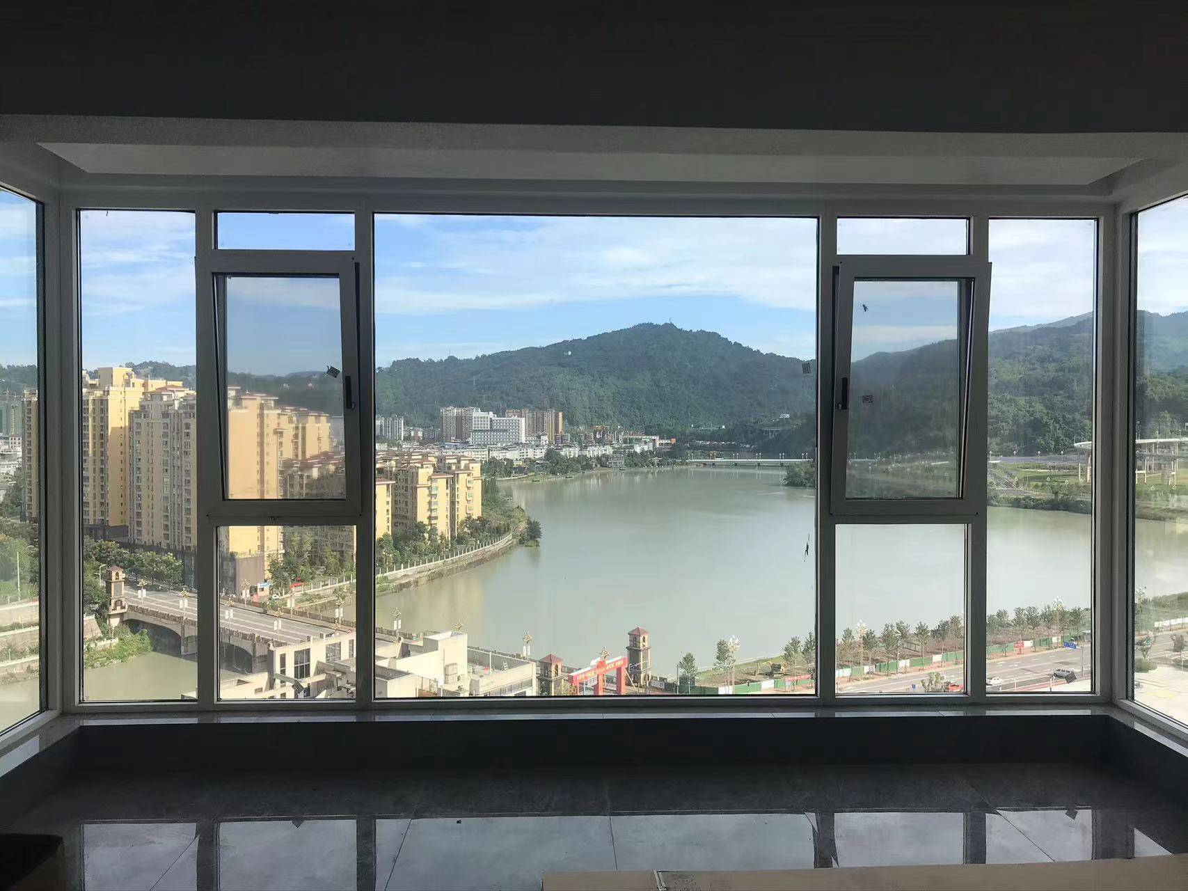 高层住宅室内视角,展示宽大的灰色断桥铝落地窗系统。中间采用大面积固定玻璃,两侧配置开启扇,最大化引入自然光线。窗外拥有开阔的江景、青山与城市建筑群,视野极佳。深